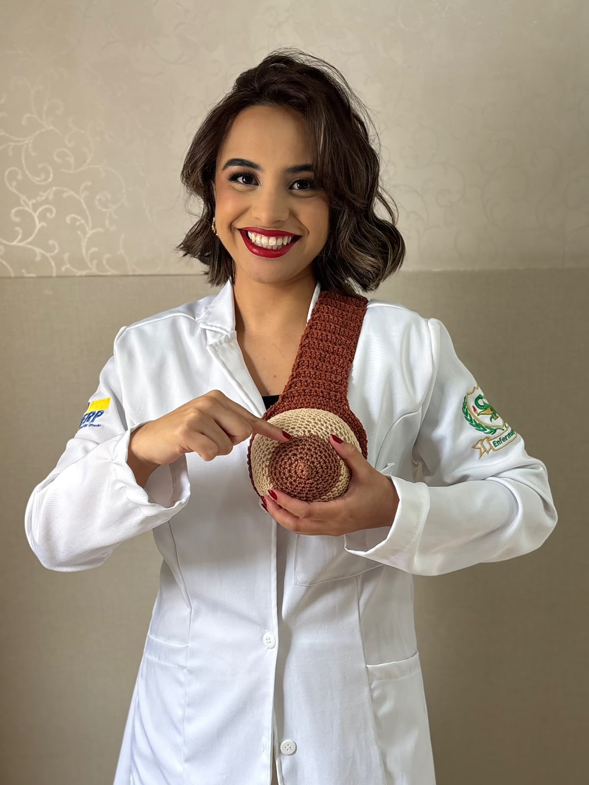 Enfermeira Ana Karolina sorrindo enquanto aponta a auréola de um modelo de mama em crochê