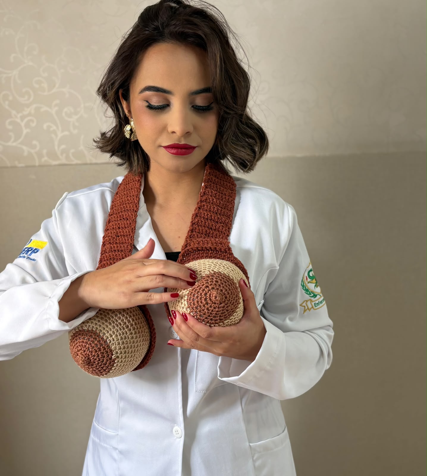 Enfermeira Ana Karolina segurando dois modelos de mama em crochê, presos a uma faixa, em demonstração
