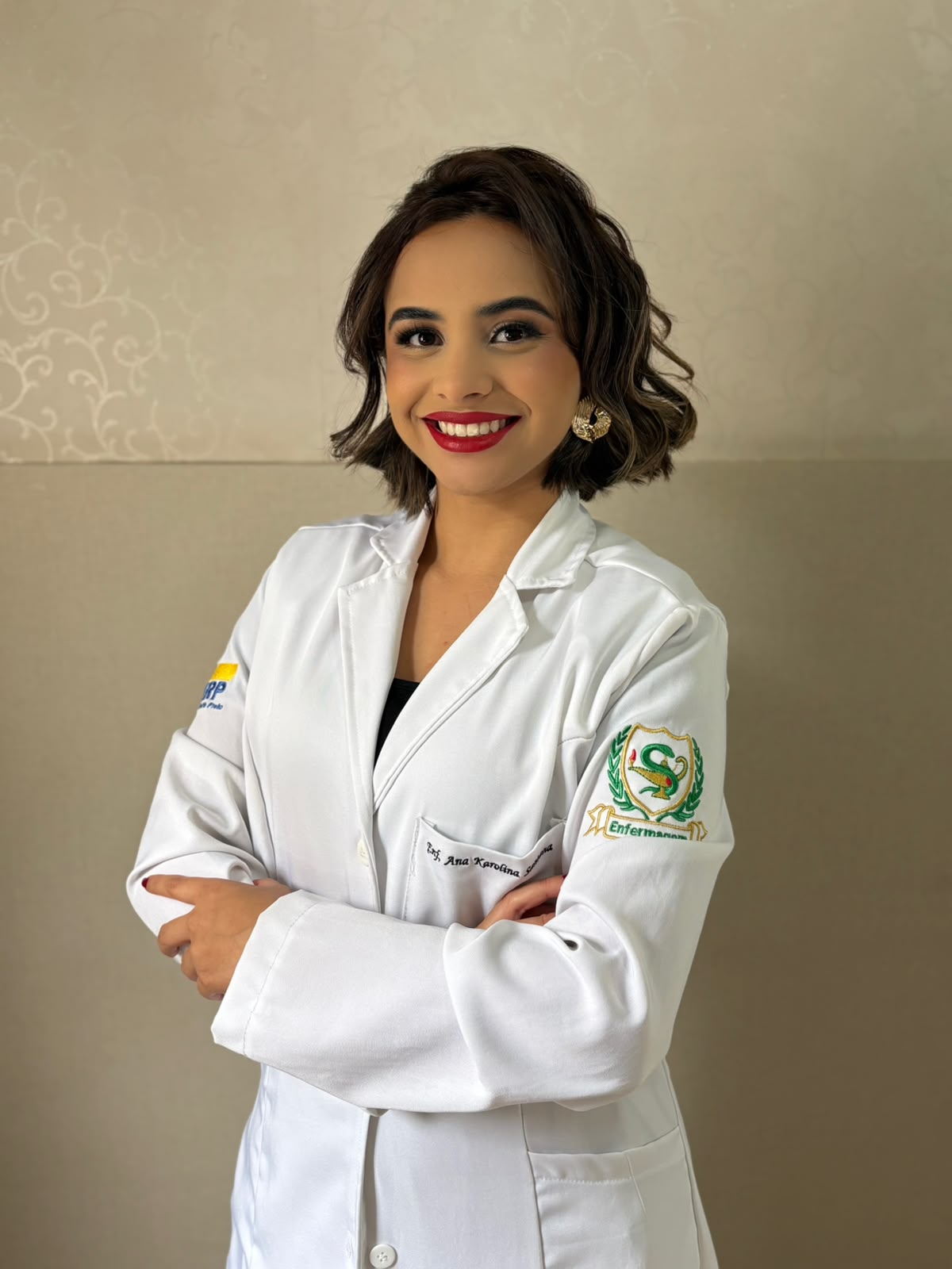 Enfermeira Ana Karolina sorrindo, de braços cruzados, em jaleco branco