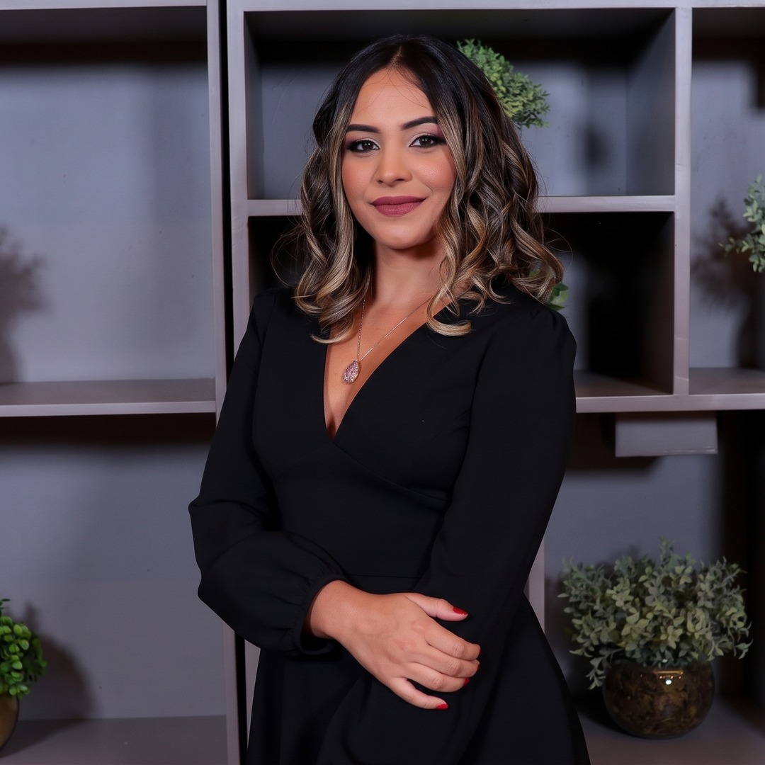 Ana Karolina, enfermeira, sorrindo de leve, de vestido preto